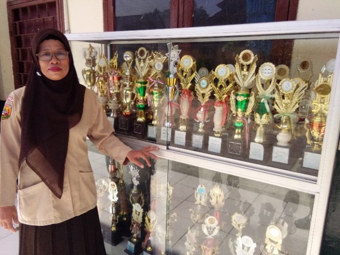 
					HJ Romlah, Kasek MI Miftahul Huda memperlihatkan sederet piala prestasi siswanya. (FOTO : Sudibyo/Harian Sederhana)