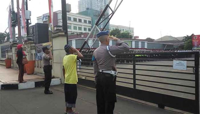 
					Kong Nur berdiri dari luar pagar sambil menatap tajam ke arah bendera merah putih yang dikibarkan oleh sejumlah petugas.