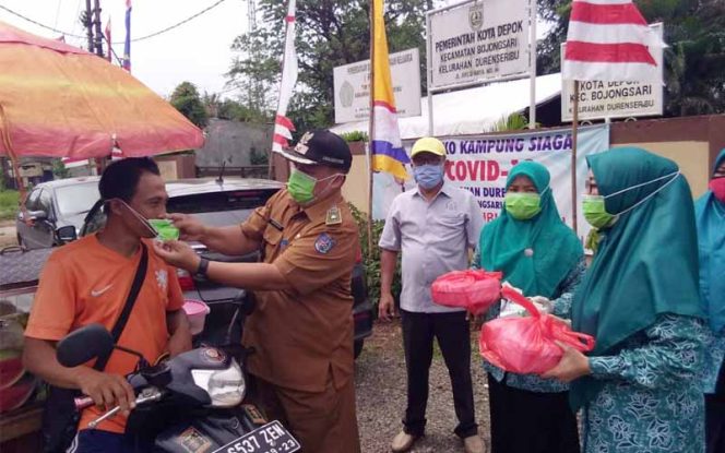 
					Lurah Duren Seribu, Suhendar didampingi Ketua PKK kelurahan setempat tengah memakaikan  masker  ke pedagang buah dan menyerahkan nasi box di tepi Jalan Arco.