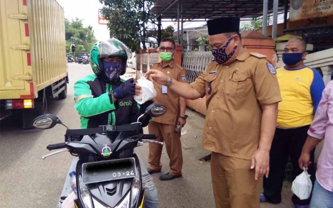 
					Lurah Pasir Putih (Pasput), Ahmad Rifa’i bagi-bagi nasi bungkus kepada ojek online dan warga pejalan kaki di depan kantor kelurahan setempat.