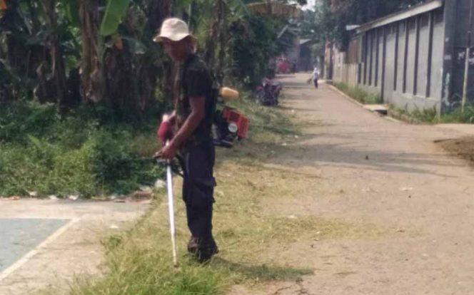 
					Sapri, petugas pemotong rumput tengah membabat rumput tepi jalan di lingkungan RW 03.